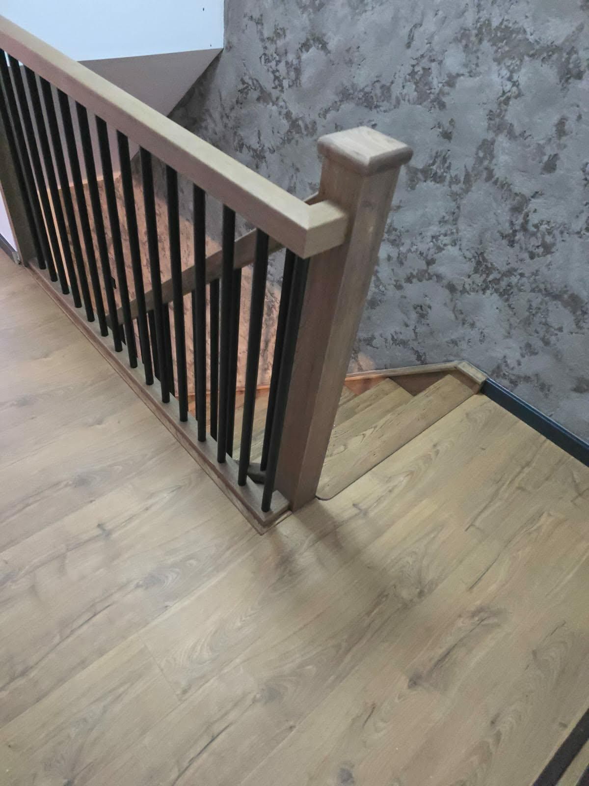 Close-up of an oak newel post with black metal spindles on a stair landing