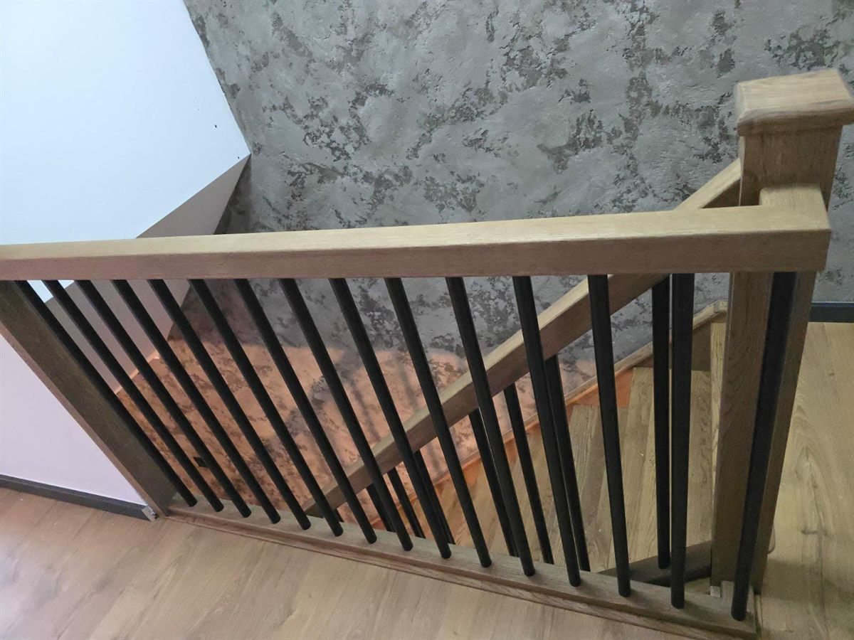 Angled view along a row of black metal balustrade spindles under an oak handrail