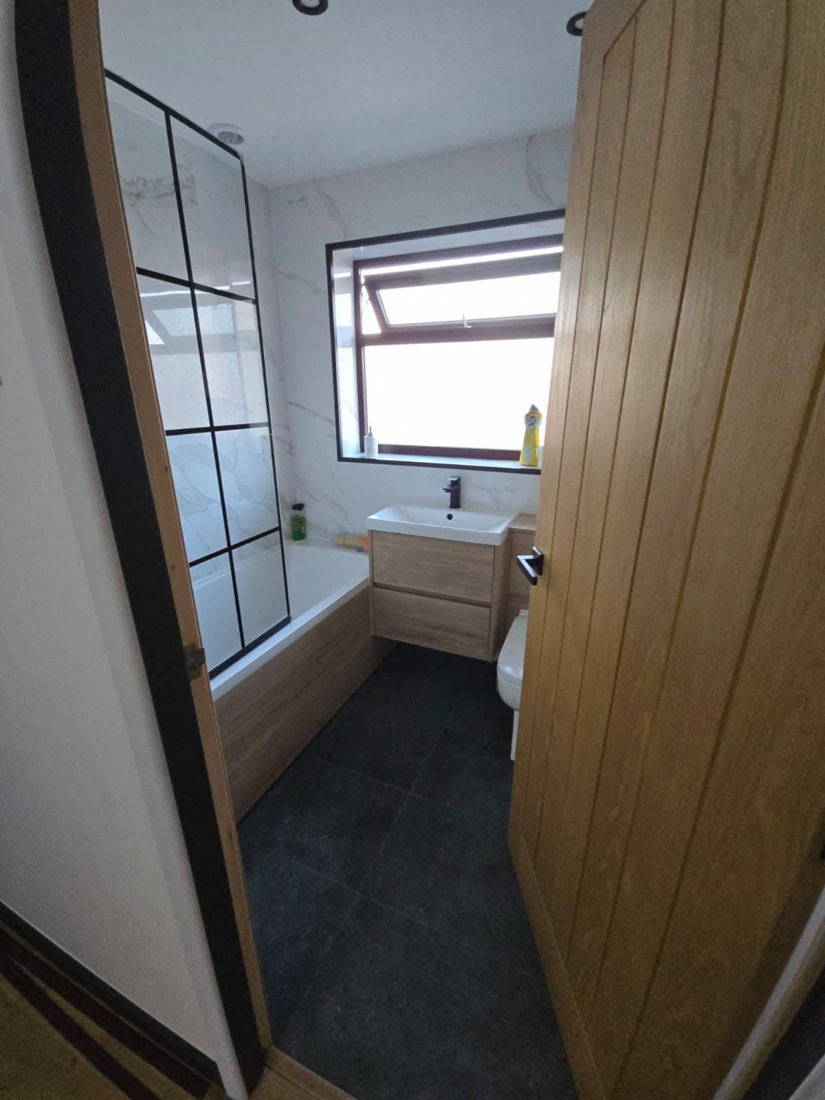 Bathroom fit-out with oak-panelled bath, black crittall-style shower screen and slate-effect floor tiles