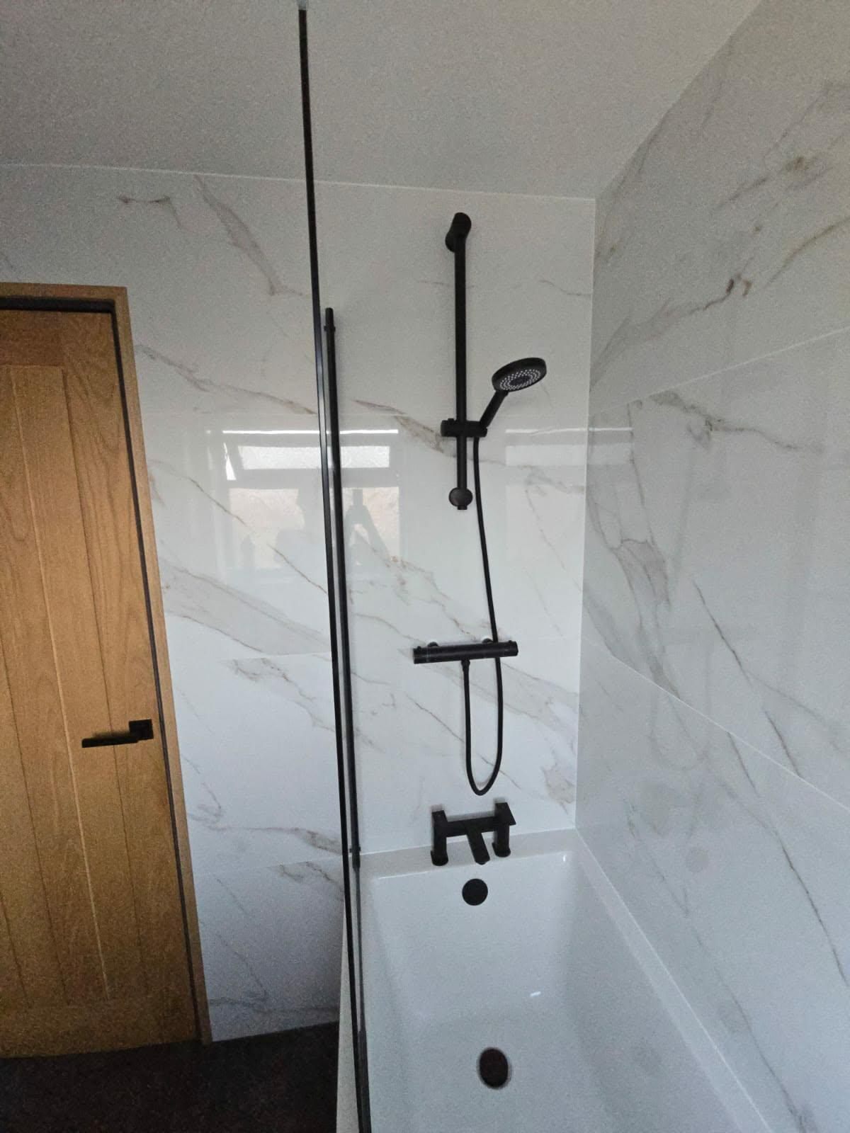 Black shower and bath taps fitted against marble-effect tiled walls