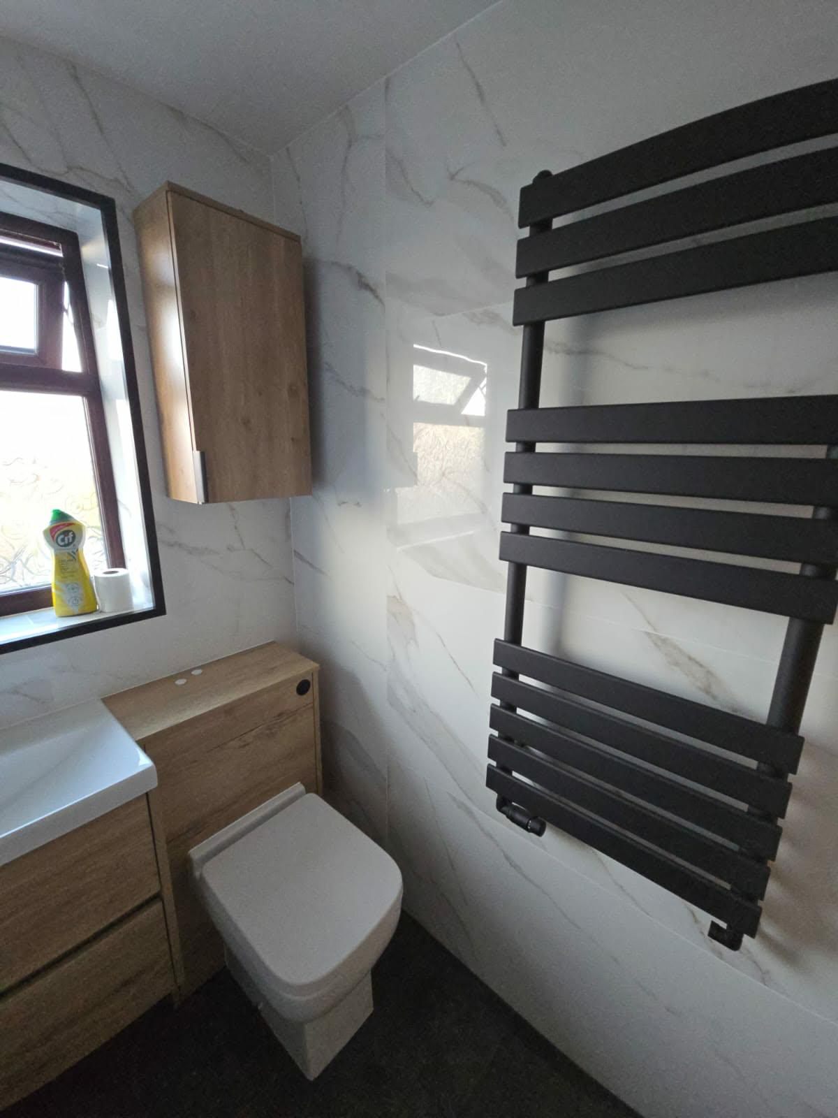 Oak wall cabinet and toilet fitted beside a black heated towel rail