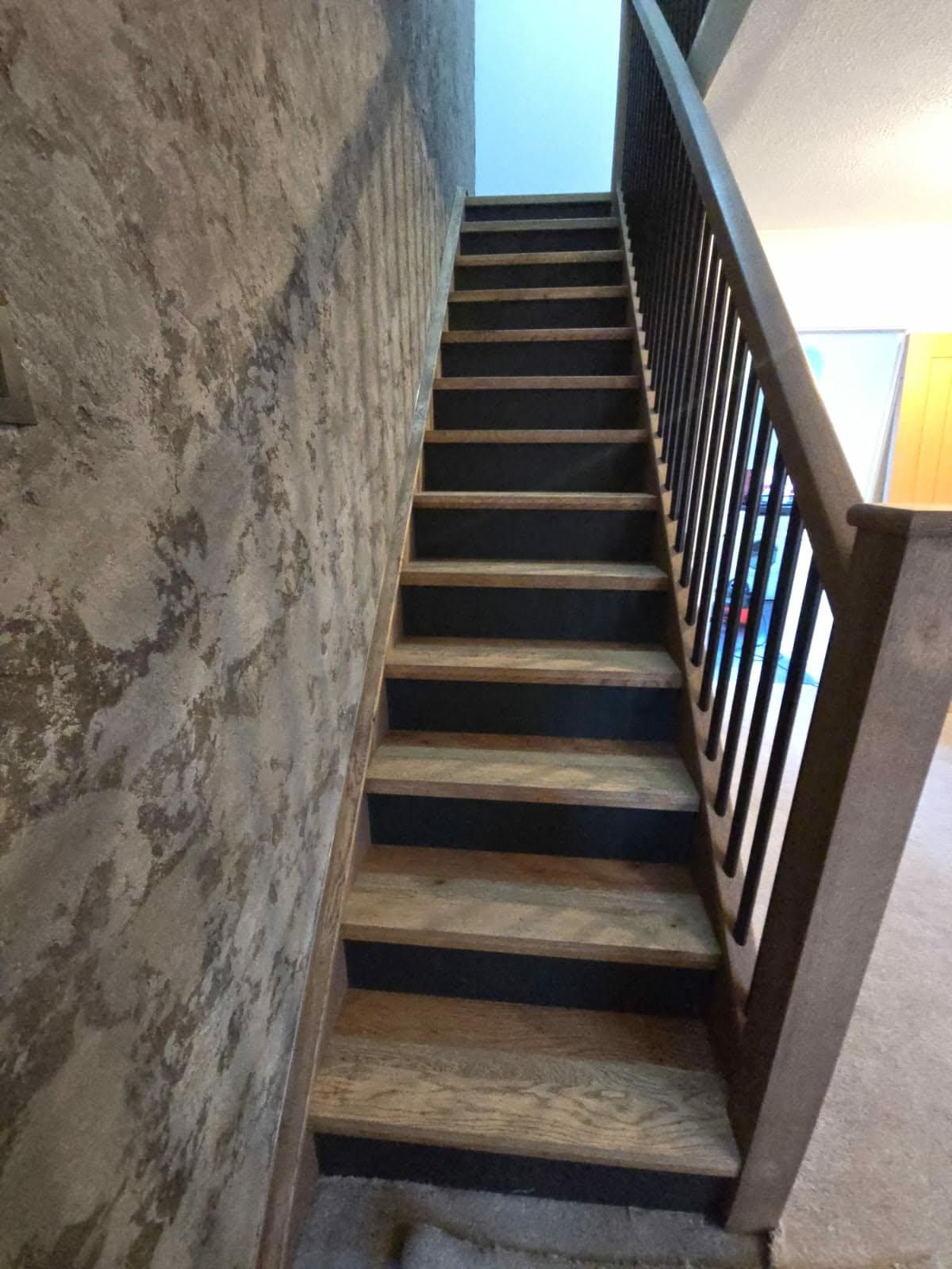 Straight flight of solid oak stair treads with dark stained risers and black metal spindles