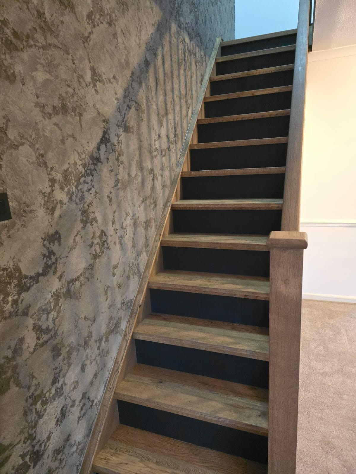 Full flight of solid oak stair treads with black riser panels and oak balustrade